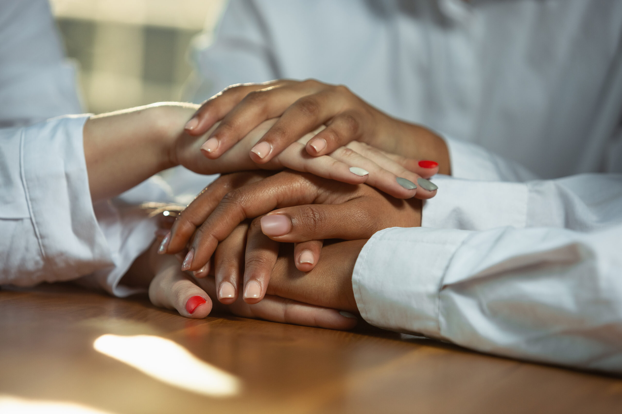 Close up of african-american and caucasian human’s hands holding on wooden table